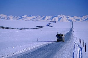 Alaska. Dalton Highway.  Arctic winter. Trans Alaska Pipeline snakes across the tundra next to a truck driving on the highway hauling freight.