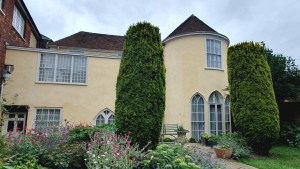"Close-up of yellow facade of rear of house, showing the routund to the right, the red tils and three arch windows on the lower floor."