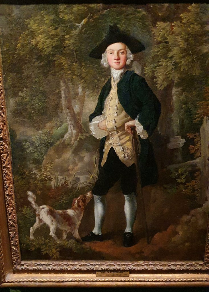 "Georgian man with triangular hat, black long coat, gold waitscoat and dog at his fee, surrounded by trees."