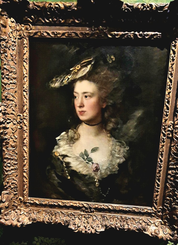 Single top of woman, elegant hat and dark dress with white silk ruff and a rose tucked into this."